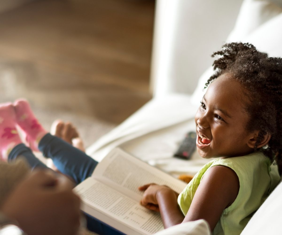 Little girl sitting on a sofa reading a book