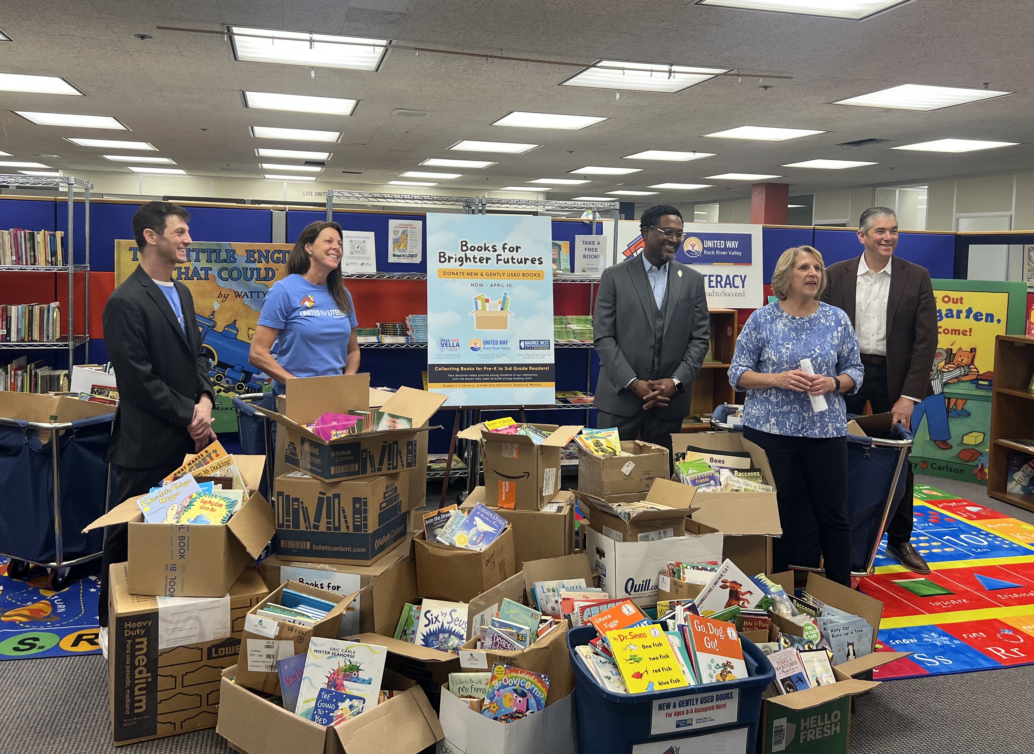 State Representatives Dave Vella and Maurice West join United Way Rock River Valley staff and community partners surrounding dozens of boxes and bins overflowing with donated children's books collected during the Books for Brighter Futures drive.