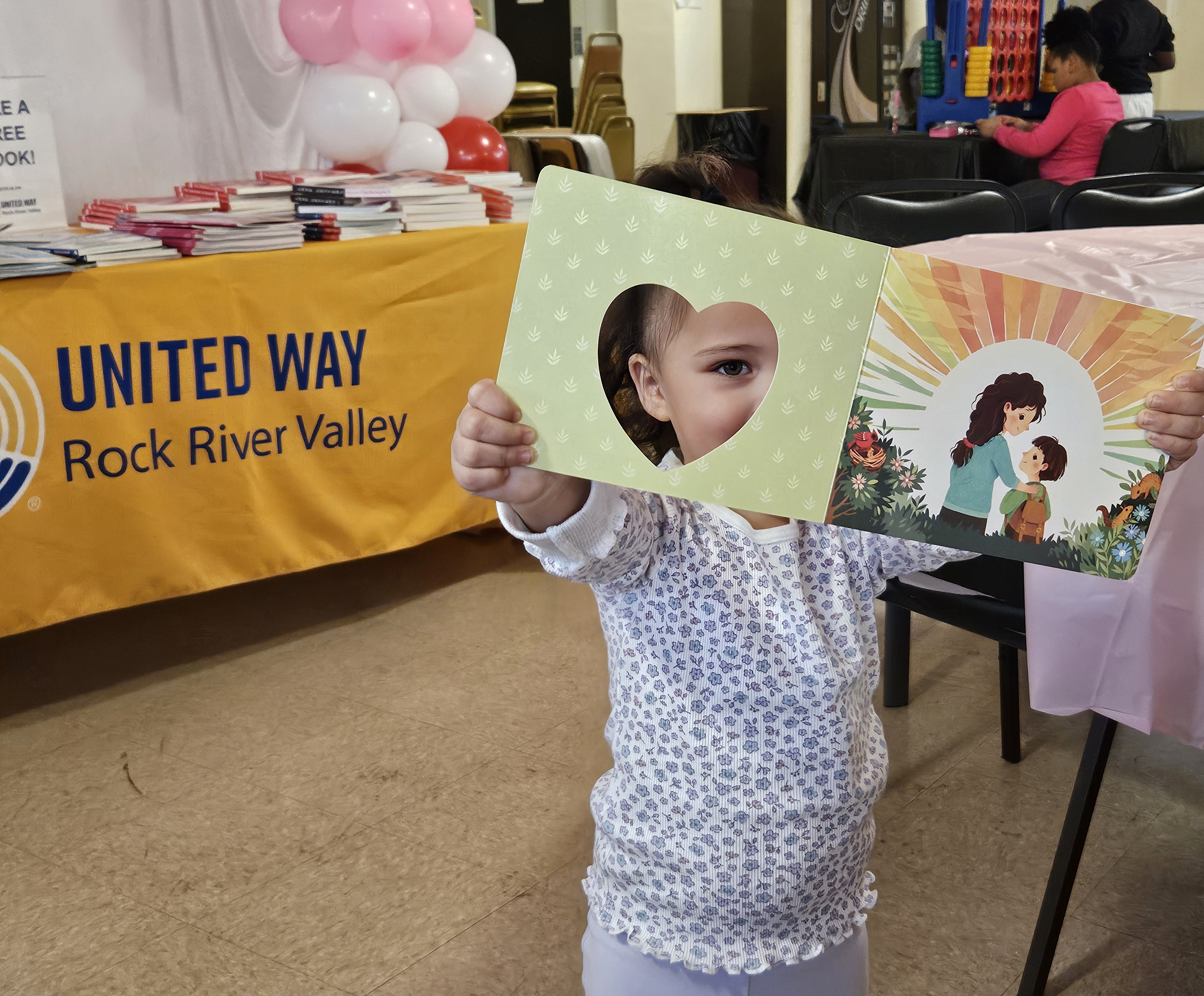 Child holding a heart-shaped book, representing early literacy and community support