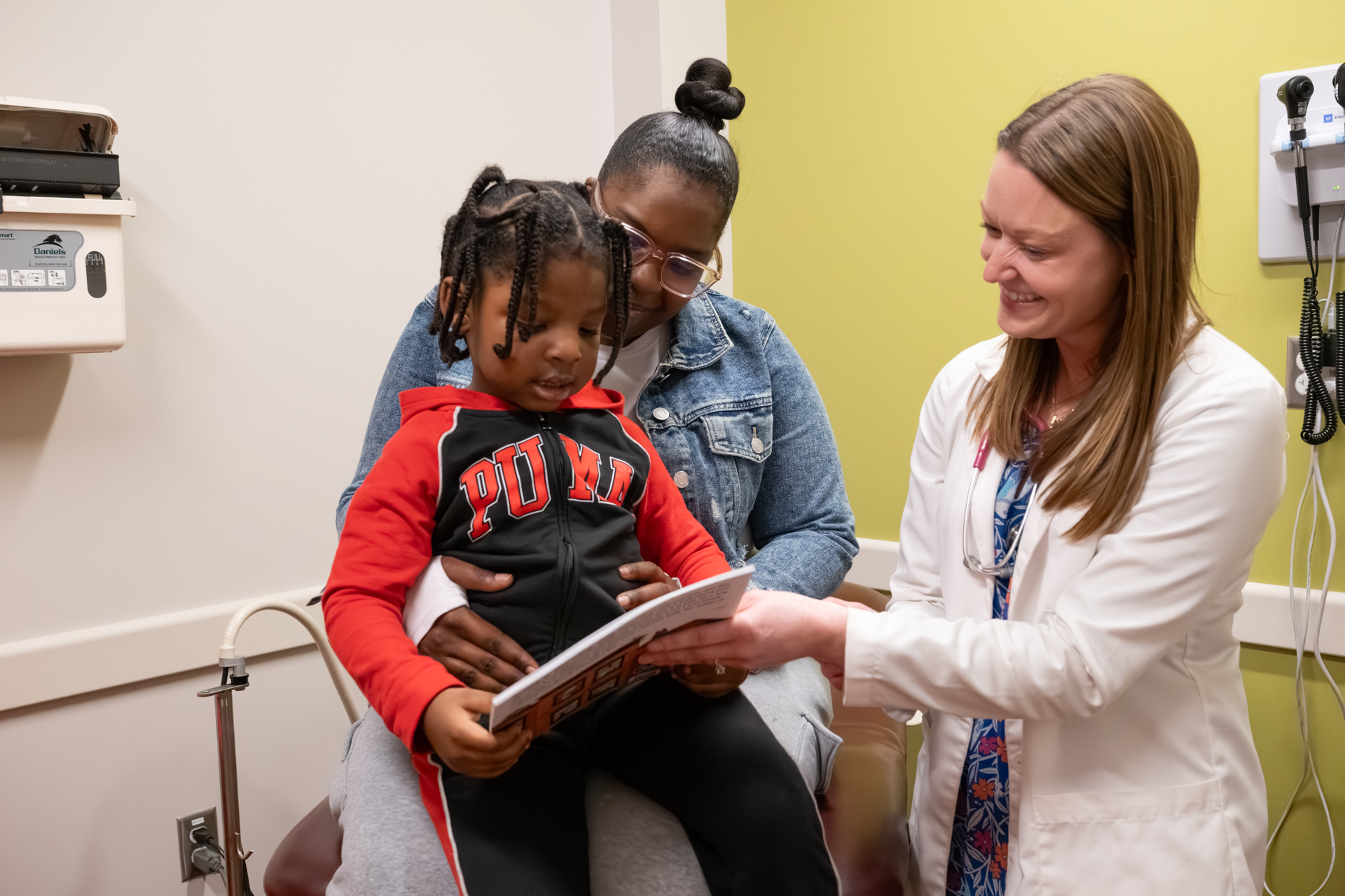 A Crusader Community Health provider reads with a young child and her caregiver during a pediatric checkup through the Reach Out & Read program at a Winnebago County clinic.