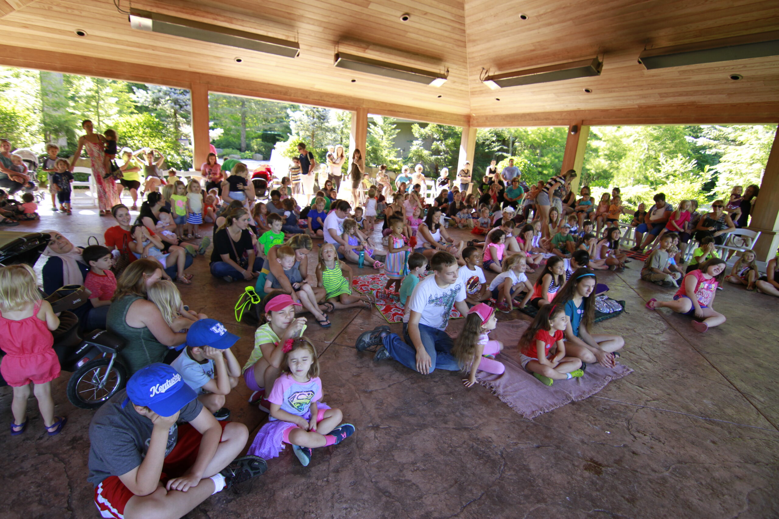 Children and caregivers gathered under an open-air pavilion at Anderson Japanese Gardens in Rockford, Illinois for an outdoor story time event, surrounded by lush summer greenery.