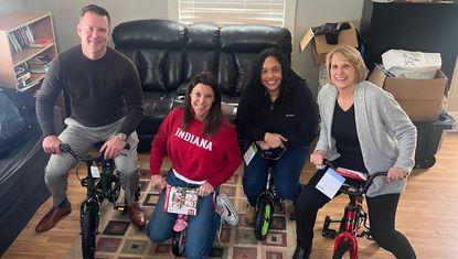 Julie Bosma, Jessica Iasparro, Roger Raley, and Sara Tusler sit on donated children’s bicycles at United Way’s Irving Avenue Strong Neighborhood House during a community donation event in Rockford, Illinois.