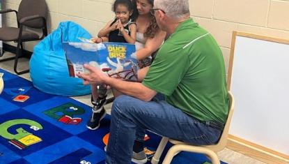 Early literacy in action. A volunteer reads a book to a child and their mother in a Ready to Learn environment set up by Rockford Alignment