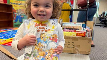 A young girl smiles holding an Arthur book she selected at the event.