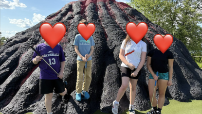 Healing Hearts 815 members playing mini golf in front of a volcano-themed obstacle at their annual outing to Volcano Falls, faces covered by hearts for privacy.